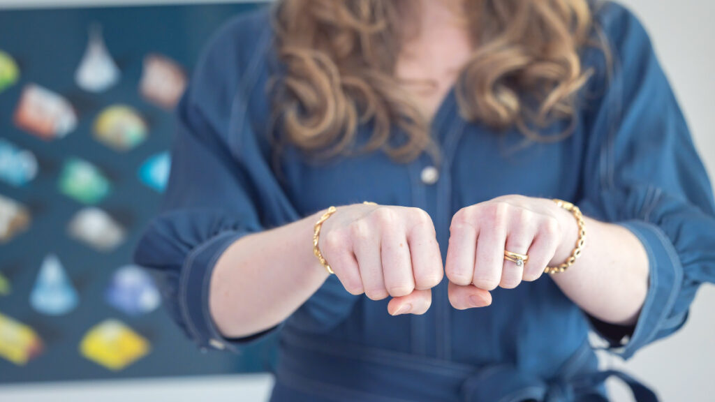 Dr Kathryn Kissell holds two closed fists side by side, distinct but touching — illustrating differentiation, the capacity to be distinct and connected at the same time.